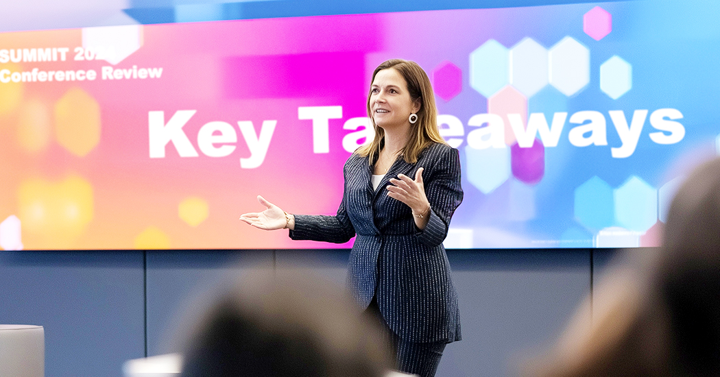 A woman in a dark suit gestures while speaking in front of a large screen displaying the words Key Takeaways during a conference or presentation.