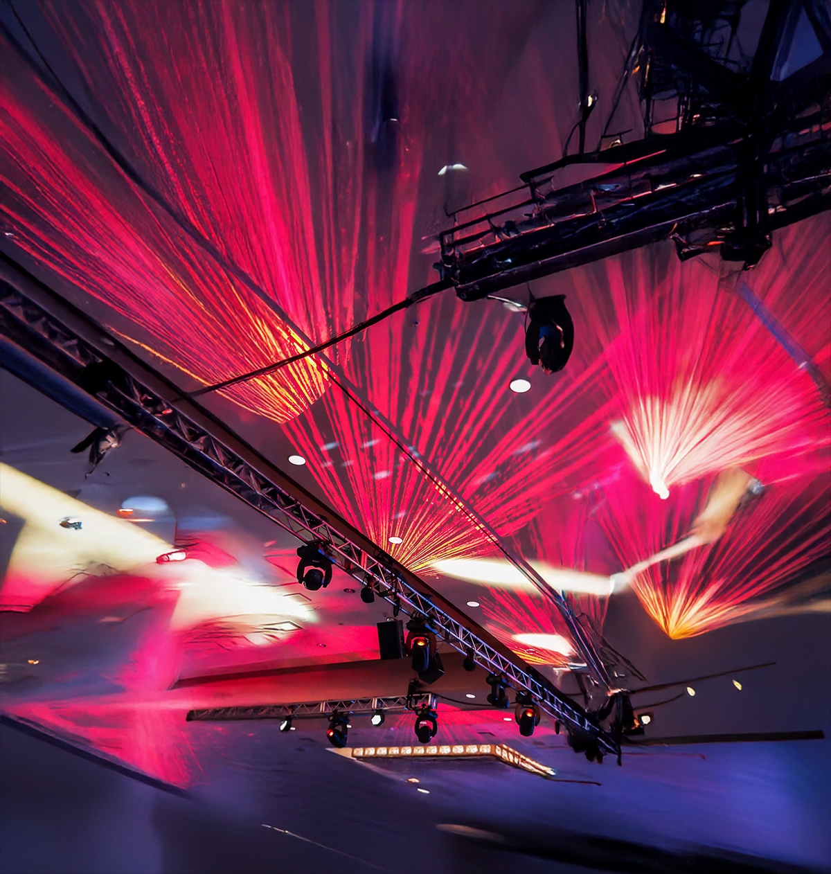Red and pink laser lights project dynamic beams and patterns across a dark ceiling, with stage lighting equipment and metal trusses in view, creating a vibrant, energetic atmosphere.