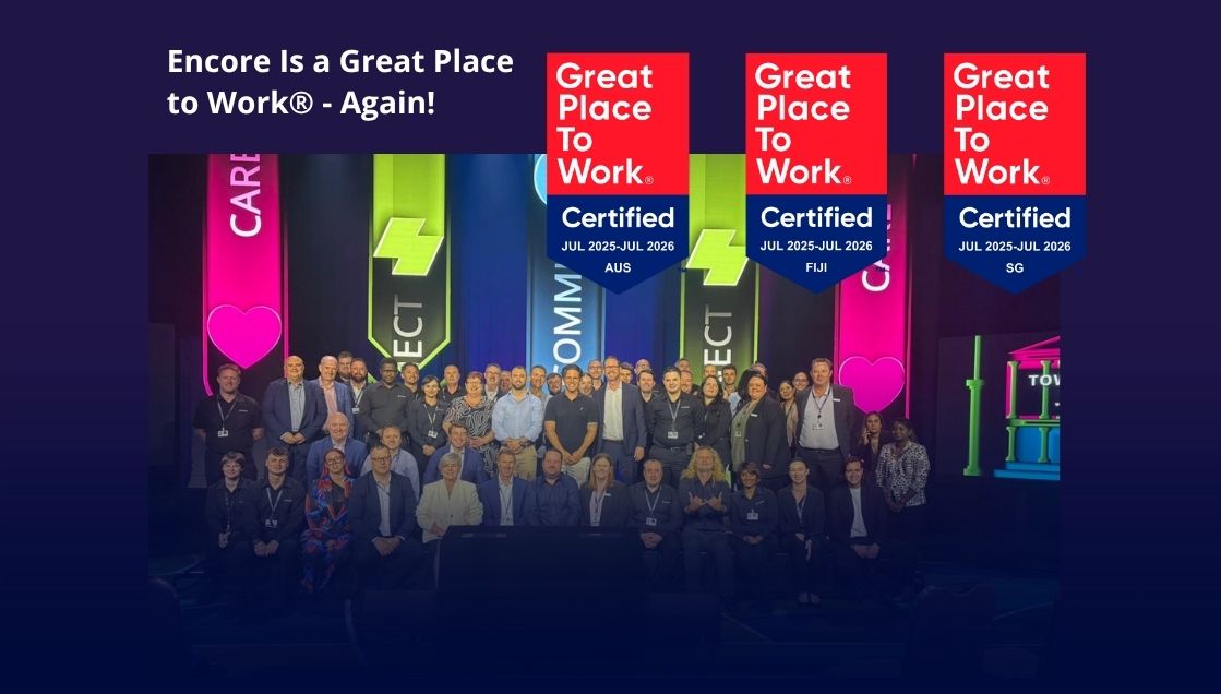 A large group of professionally dressed people pose on stage in front of colorful banners. Text reads “Encore Is a Great Place to Work® – Again!” with three “Great Place to Work Certified” badges for AUS, Fiji, and SG.