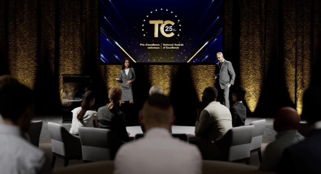 A woman and a man stand on a stage in front of an audience, with a large screen behind them displaying 25 TC and National Awards of Excellence in a formal event setting.