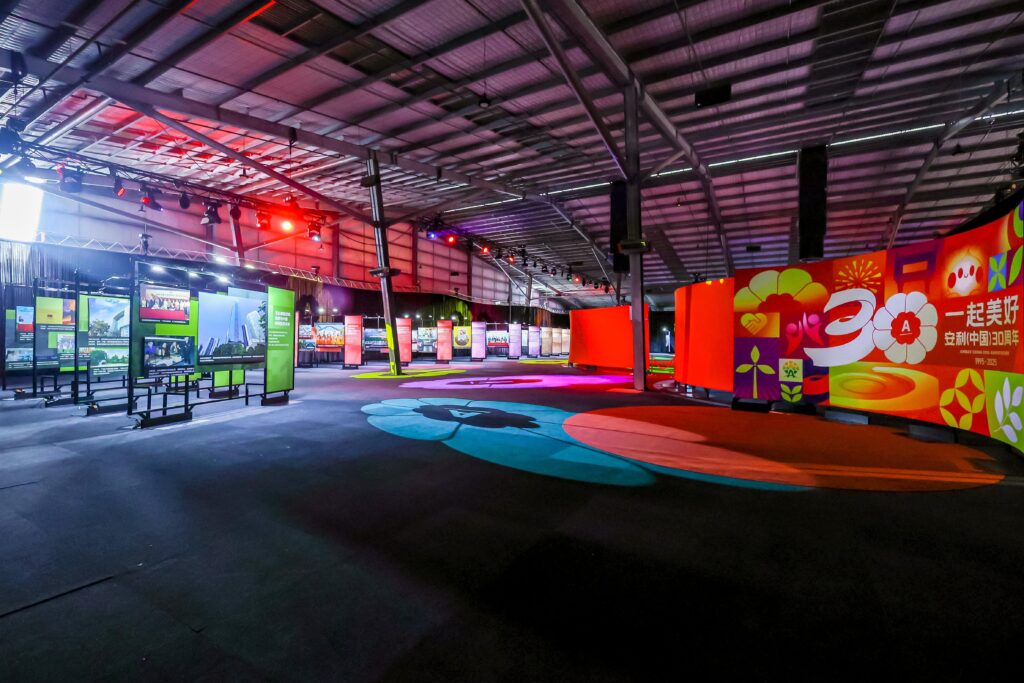 A spacious indoor exhibition hall with colorful graphic displays and large, vibrant floor art under bright lighting, showcasing exhibits along the walls and banners with Chinese characters.