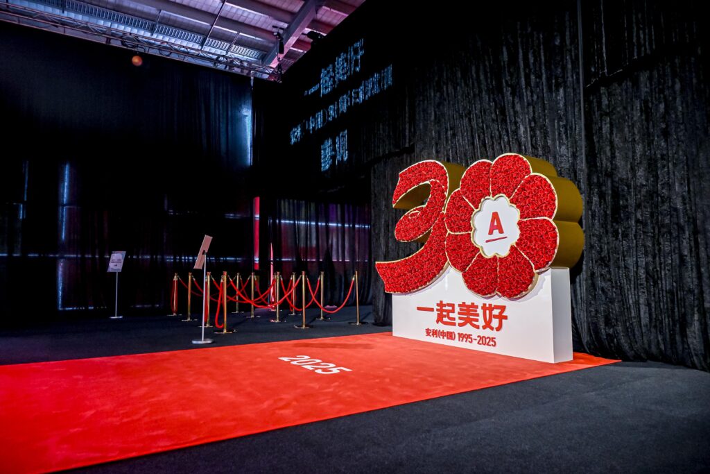 A large floral sculpture with the number 30, the letter A, and red accents stands on a red carpet labeled 2025 in an indoor event space with dark curtains and roped barriers.
