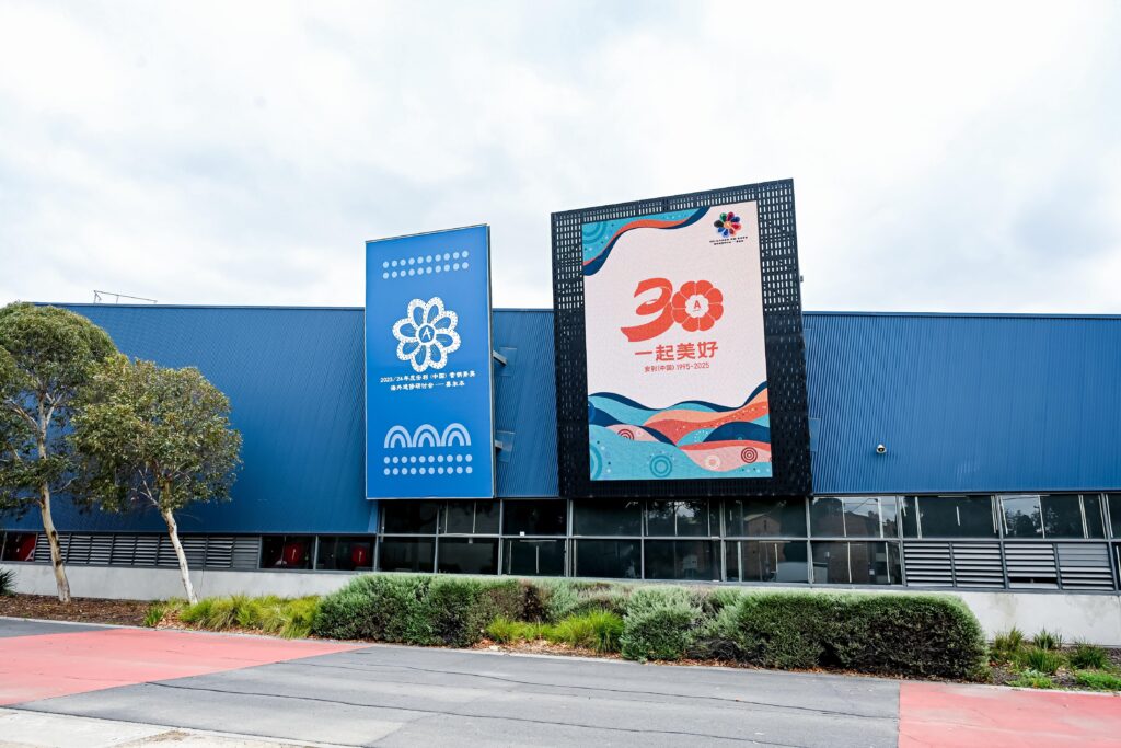 A blue building with two large banners, one featuring a floral design and the other displaying “30” with colorful graphics and Chinese characters, surrounded by greenery and a tree.