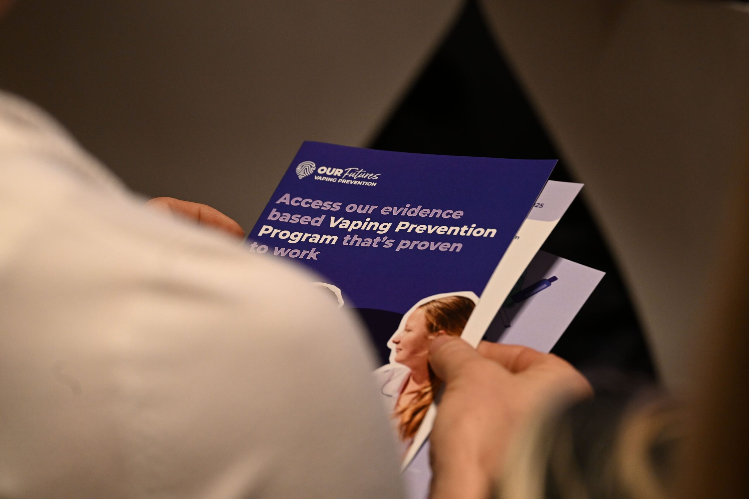 한 사람이 ADIA 2023 로고와 어린 소녀의 사진이 표지에 있는 '효과가 입증된 증거 기반 베이핑 예방 프로그램 이용하기'라는 제목의 브로셔를 들고 있습니다.