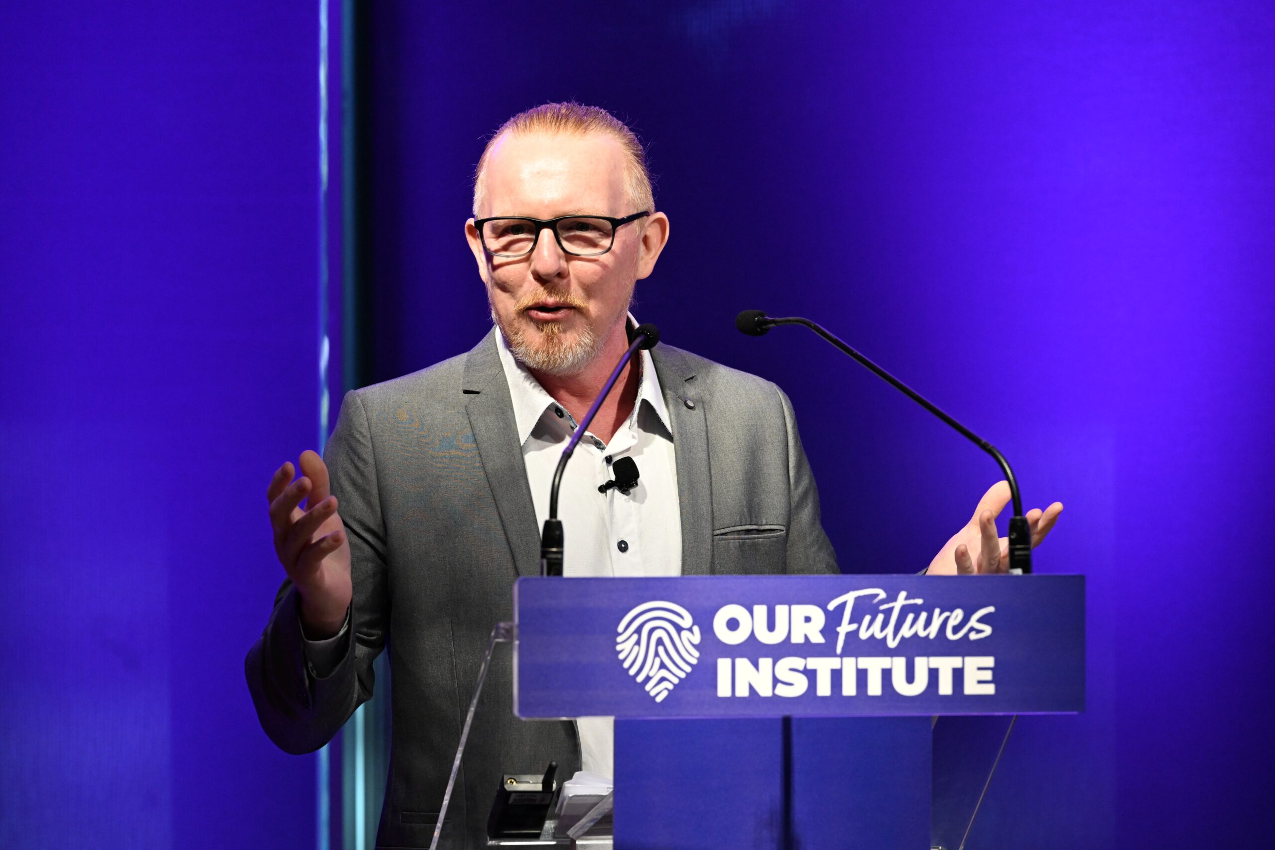 보라색 조명이 켜진 배경에서 안경과 상투를 튼 한 남성이 '우리의 미래 연구소'라고 적힌 ADIA 2023 연단에서 손으로 제스처를 취하며 연설하고 있습니다.
