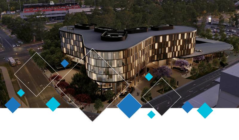 A modern, multi-story building with curved architecture is illuminated at dusk, surrounded by trees, roads, and parking lots. Geometric blue and white diamond shapes overlay the lower part of the image. WSCC