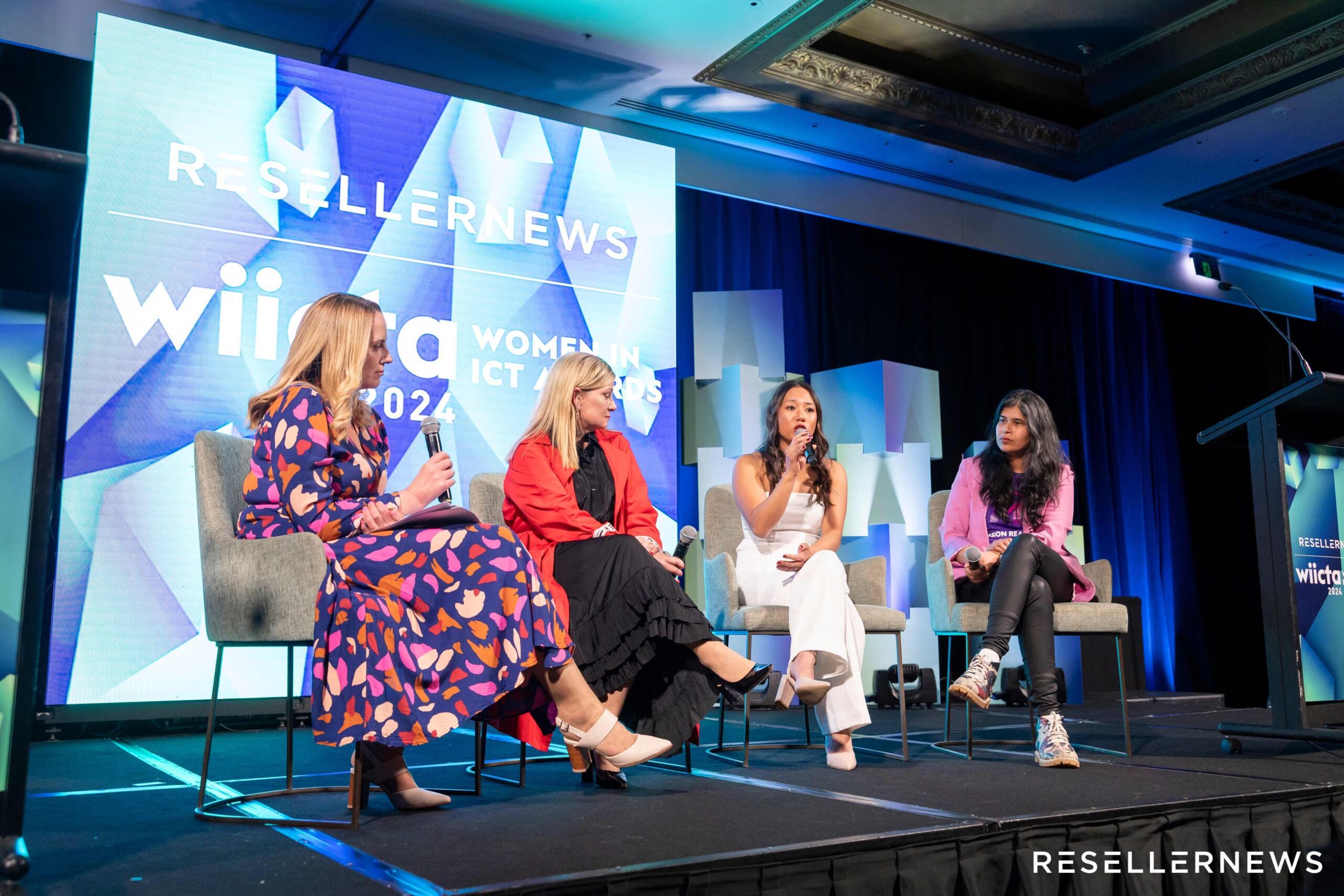 Four women sit on stage, engaging in a panel discussion at the WiICT (Women in ICT) event, with Reseller News branding displayed on large screens behind them.