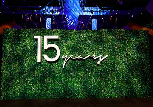 A large green wall covered with foliage displays the text 15 years in bold white lettering, showcasing expert designing event media walls for a 15-year anniversary celebration under dramatic event lighting.