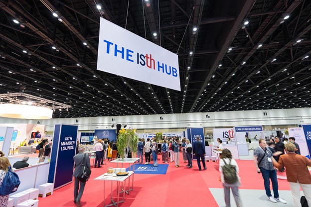 A large convention hall with attendees walking and gathering around booths; a prominent sign reads THE ISTH HUB, reflecting the busy and professional atmosphere of the ISTH 2024 Congress.