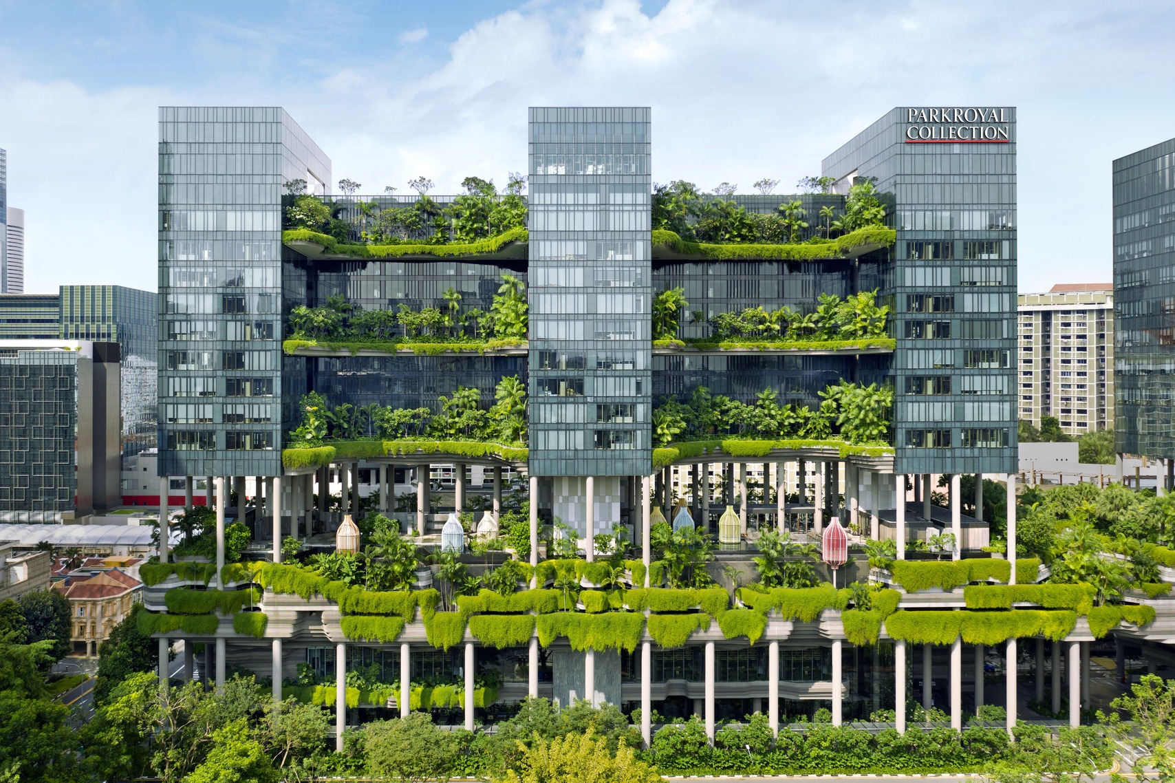 A modern multi-story building with glass facades, lush green plants, and gardens on each level is labeled PARKROYAL COLLECTION Pickering Singapore. The structure is elevated on pillars with cascading greenery throughout.