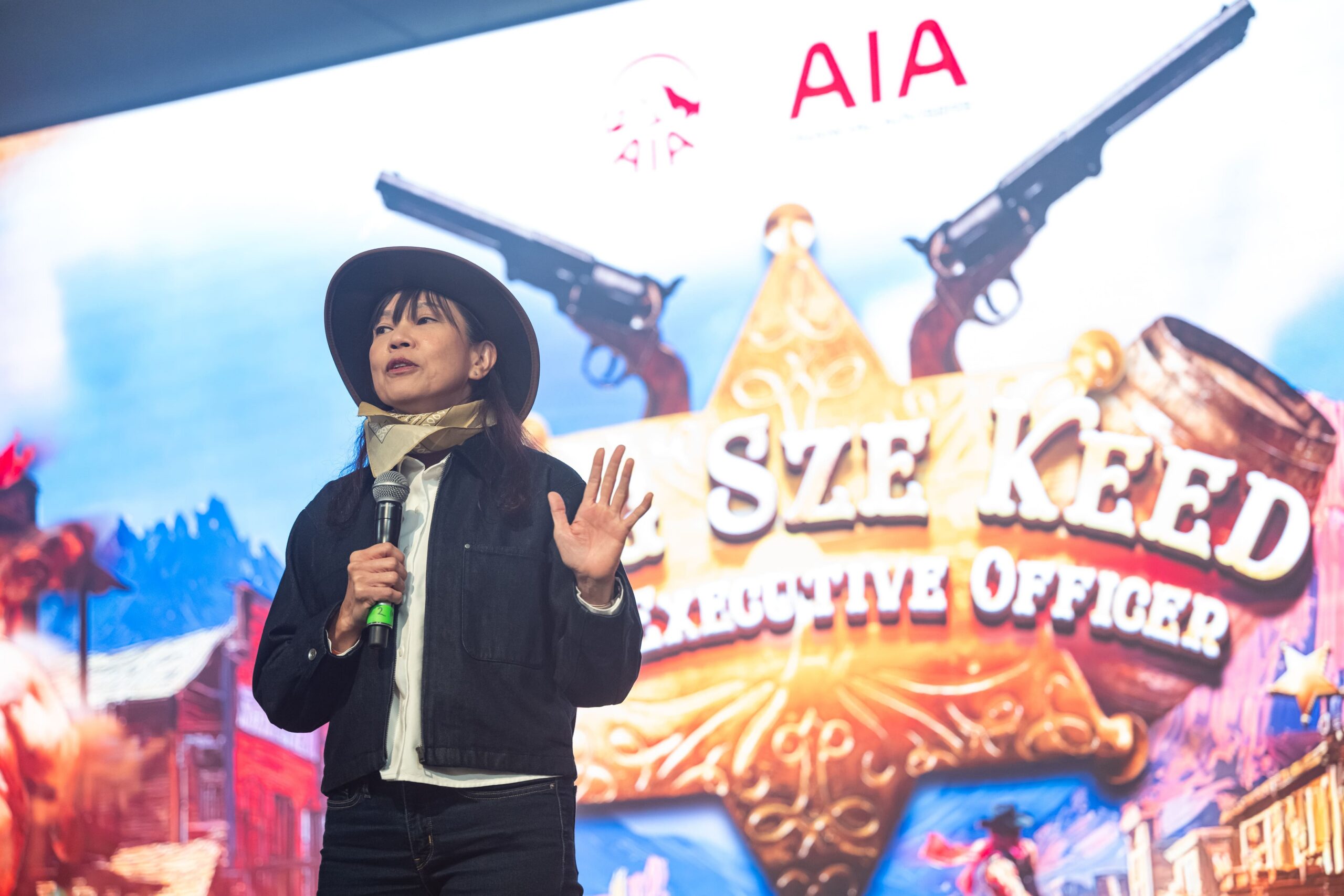 Event host speaking on stage with microphone against AIA branded western backdrop - Encore Event Technologies