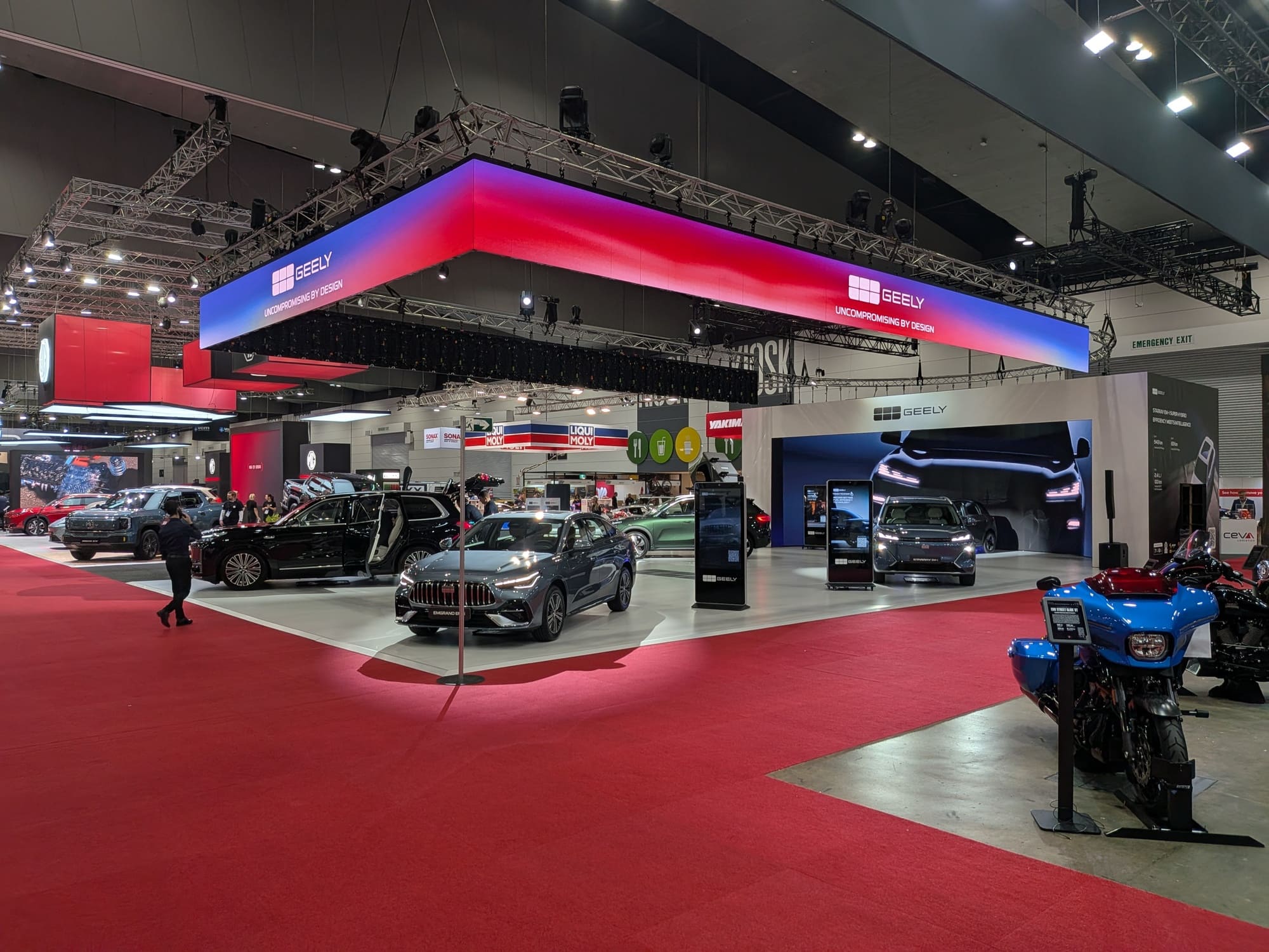 Large Geely stand under illuminated overhead signage with vehicles displayed on red carpet flooring - Encore Event Technologies