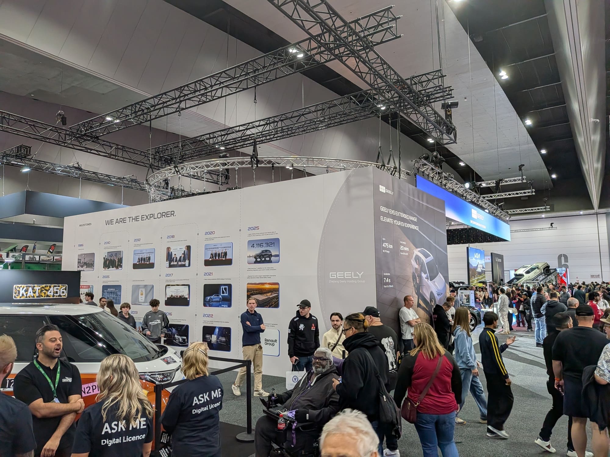 Wide view of busy motor show floor with Geely stand, overhead rigging and visitors exploring exhibition space - Encore Event Technologies
