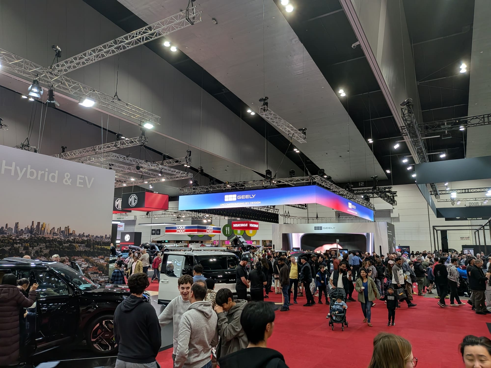 Crowded exhibition hall with Geely signage overhead and attendees exploring vehicle displays - Encore Event Technologies