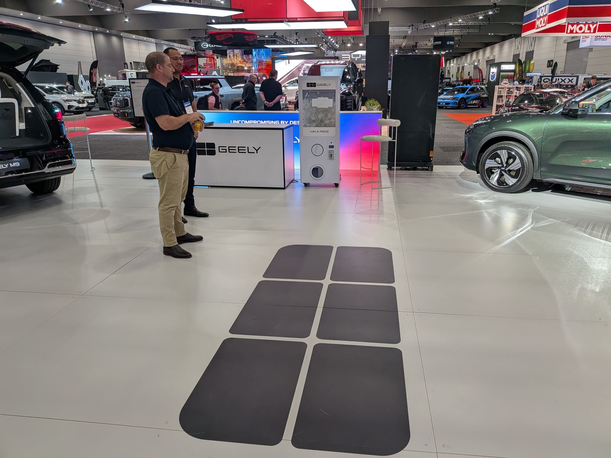 Event staff standing near Geely booth with floor decals and vehicle display in showroom environment - Encore Event Technologies