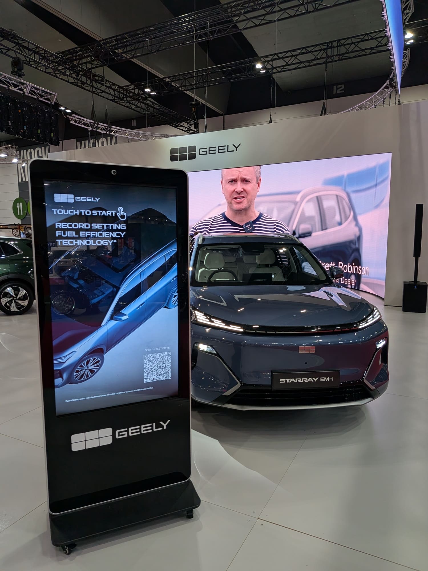 Front view of Geely vehicle with digital touchscreen kiosk and branded LED screen backdrop at exhibition booth - Encore Event Technologies