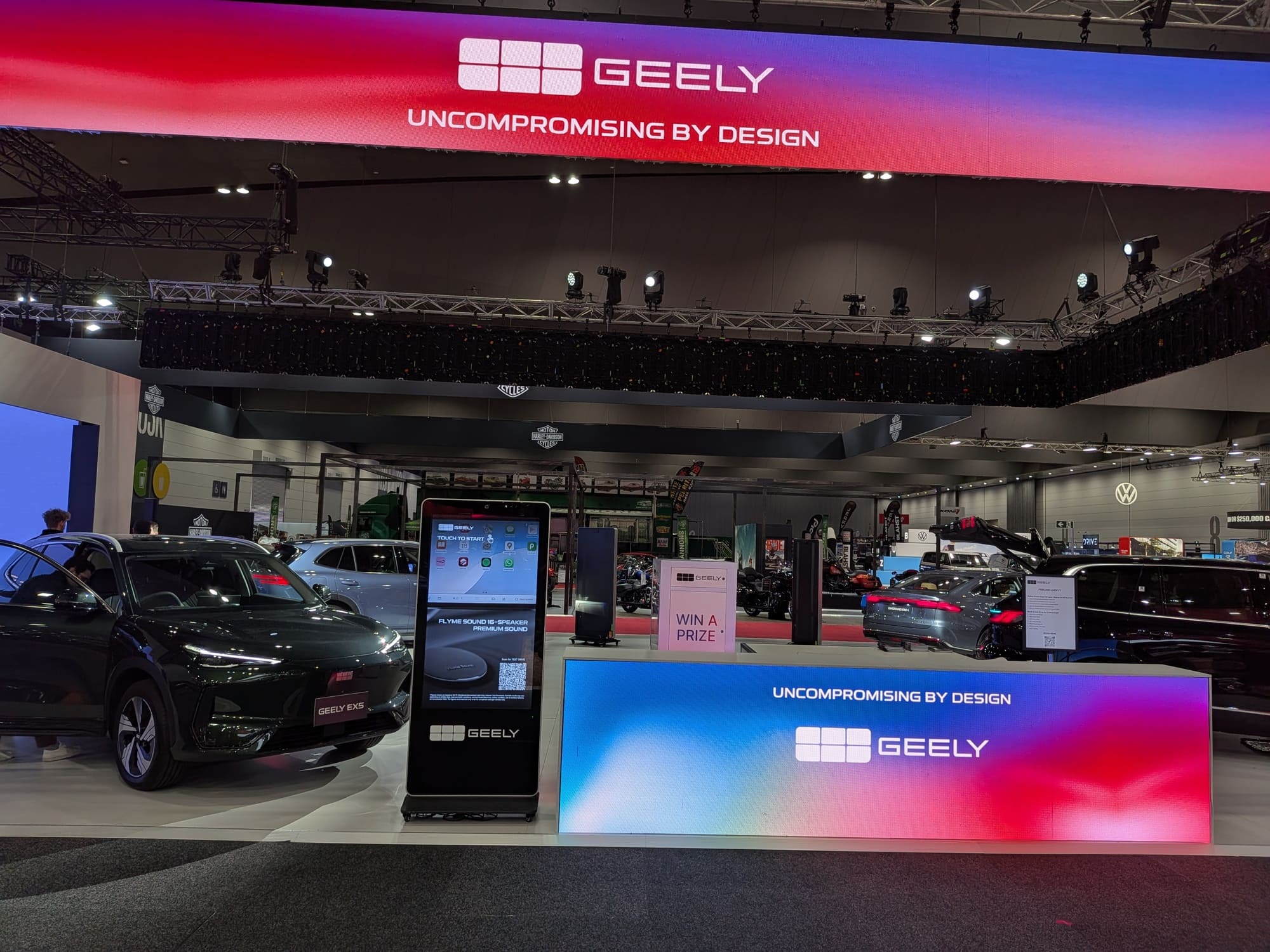 Wide view of Geely exhibition space with overhead branding banner and multiple vehicle displays - Encore Event Technologies