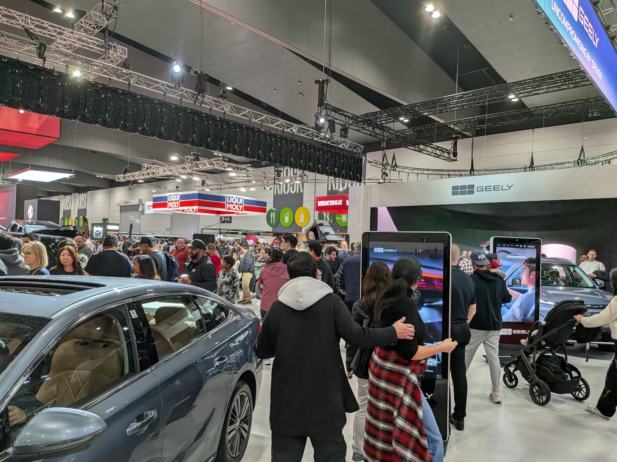 Crowd moving through Geely display with interactive kiosks and vehicle engagement zones at motor show - Encore Event Technologies