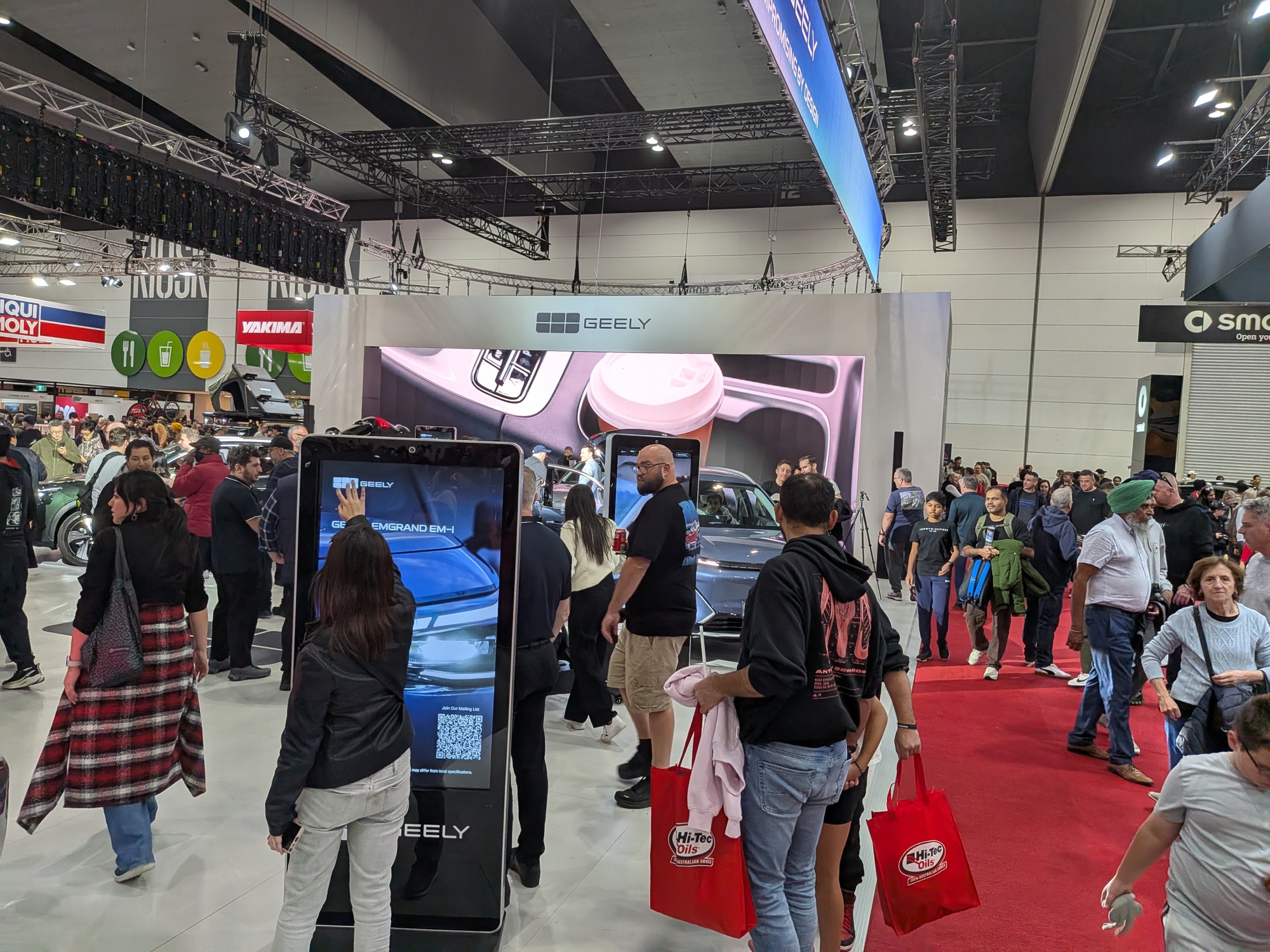 Geely activation area with touchscreen kiosks, LED wall and visitors carrying event merchandise bags - Encore Event Technologies