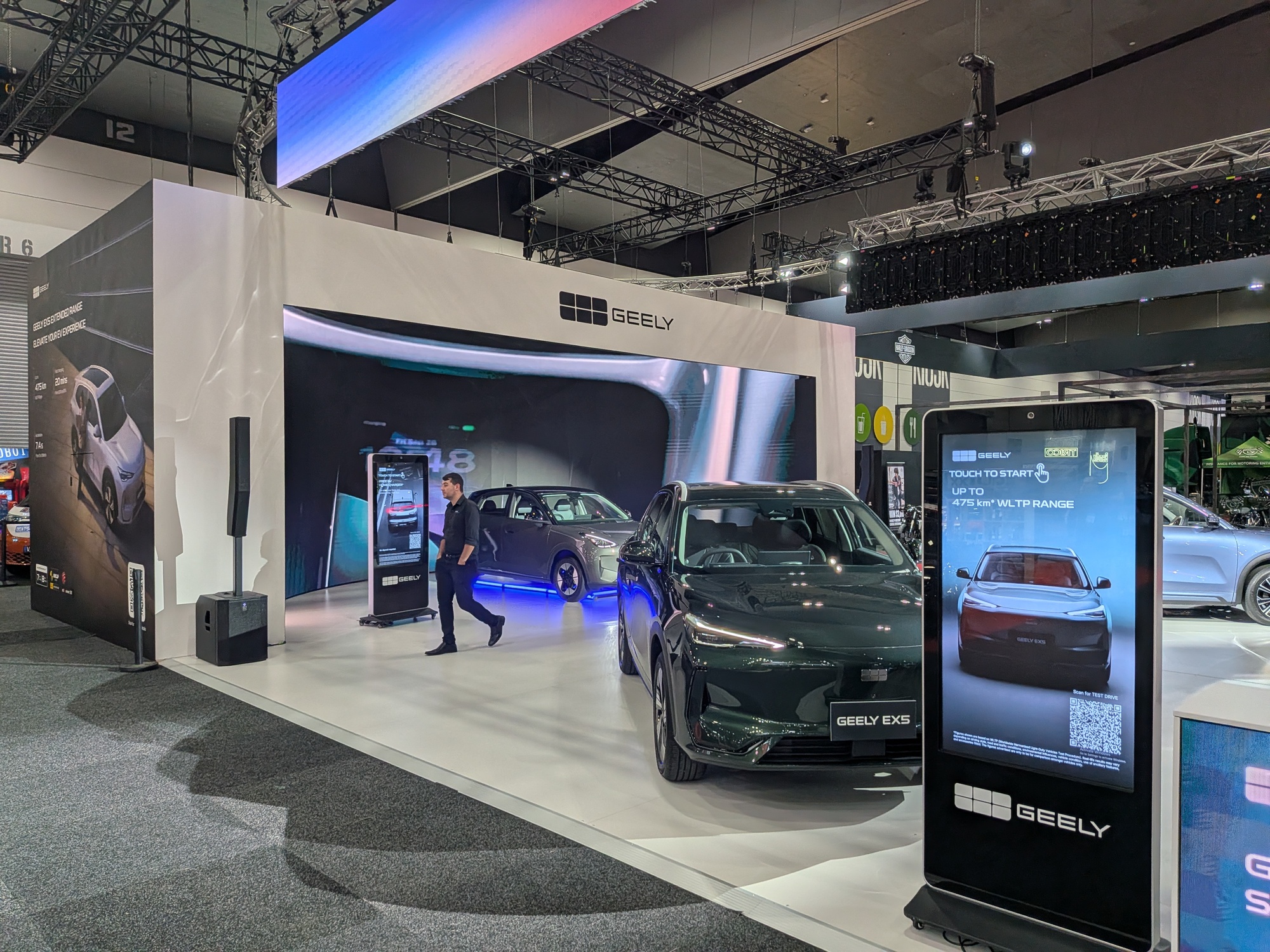 Angled view of Geely stand with vehicles, digital kiosk display and large LED screen backdrop in motor show environment - Encore Event Technologies