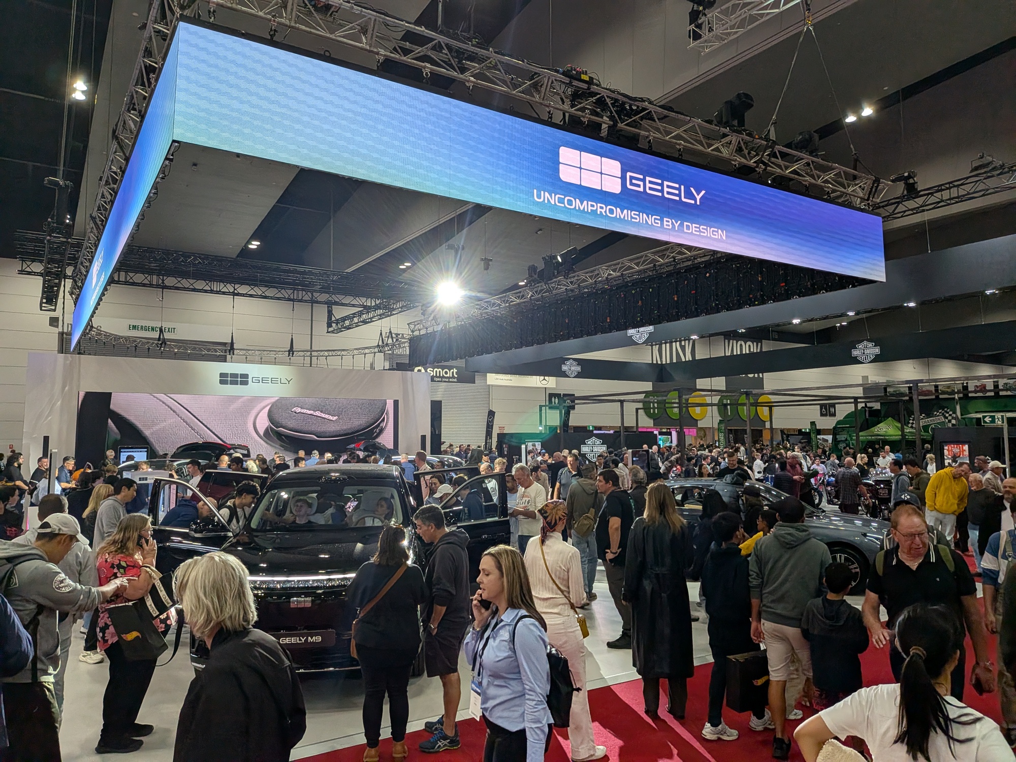 Crowded Geely display area with vehicles, open doors and overhead “Uncompromising by Design” branding banner - Encore Event Technologies