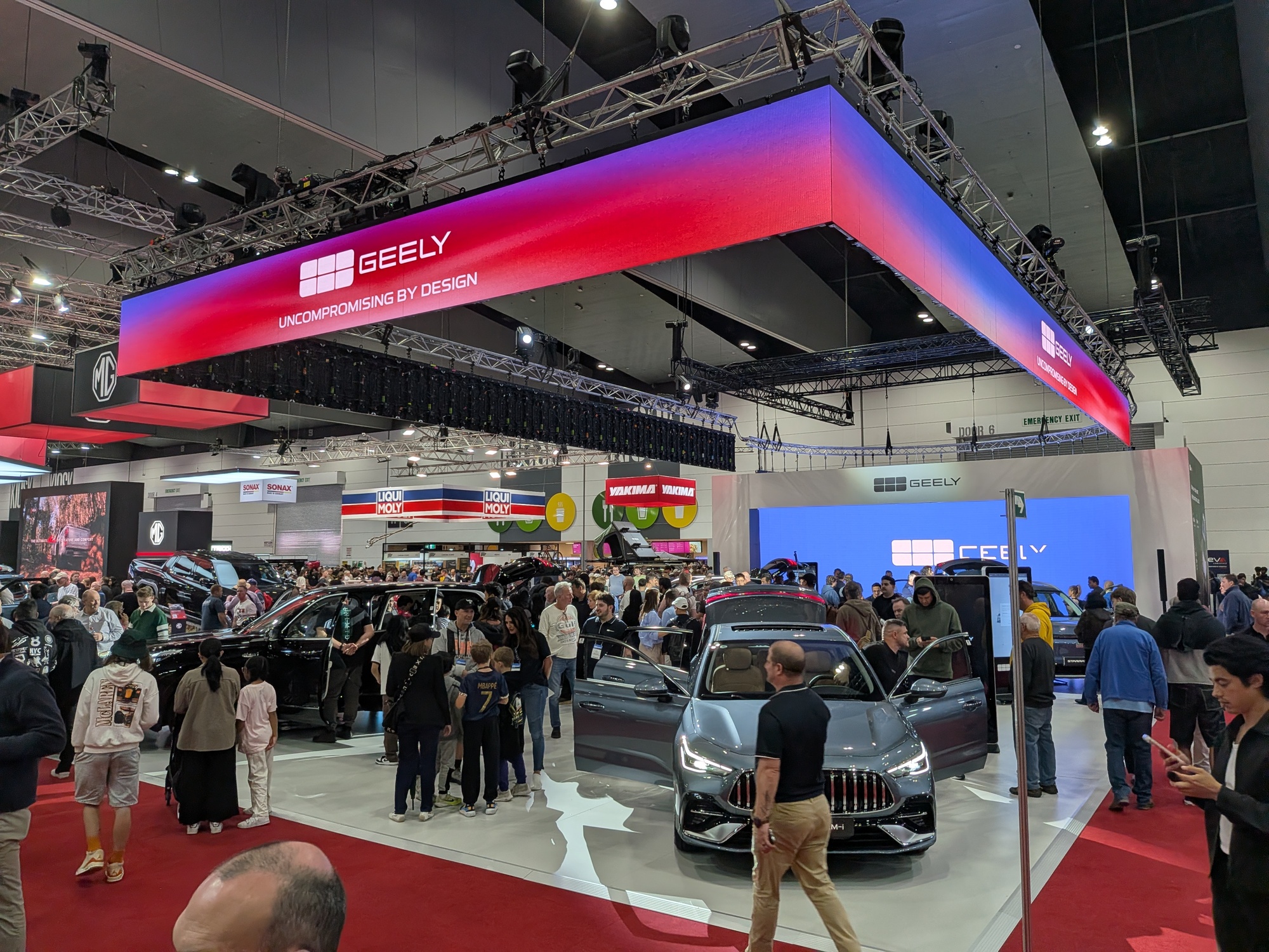 Wide shot of Geely booth with overhead branding structure, vehicles on display and high visitor traffic - Encore Event Technologies