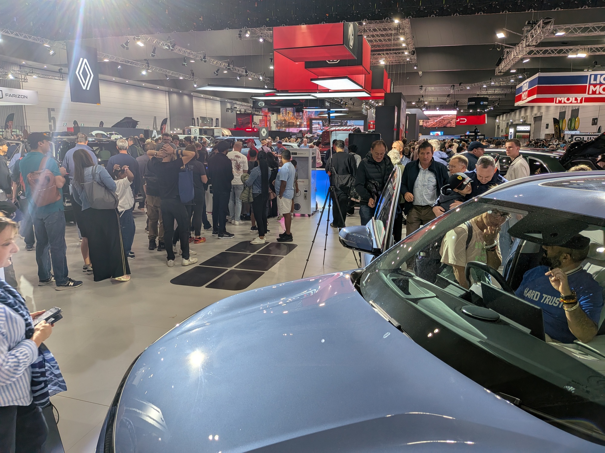 Close-up foreground of vehicle bonnet with busy exhibition floor and attendees exploring displays in background - Encore Event Technologies