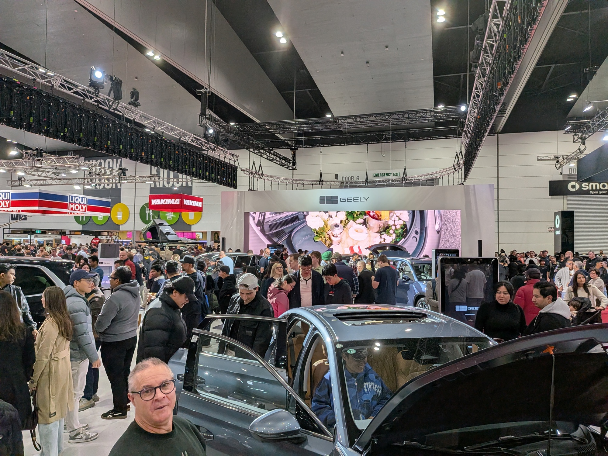 Geely stand with large LED screen featuring lifestyle imagery, vehicles displayed and attendees interacting on floor - Encore Event Technologies
