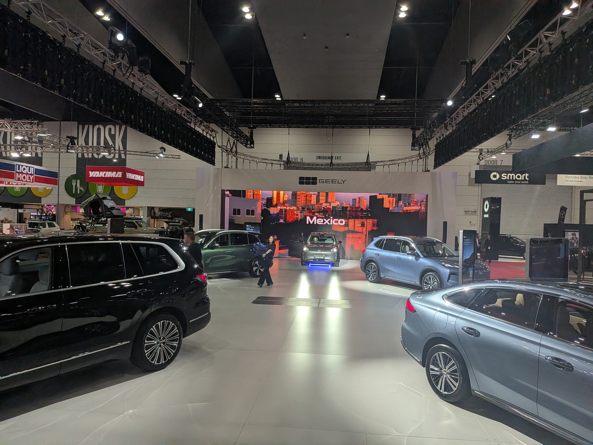 Geely stand with multiple vehicles positioned around large LED video wall displaying city backdrop - Encore Event Technologies
