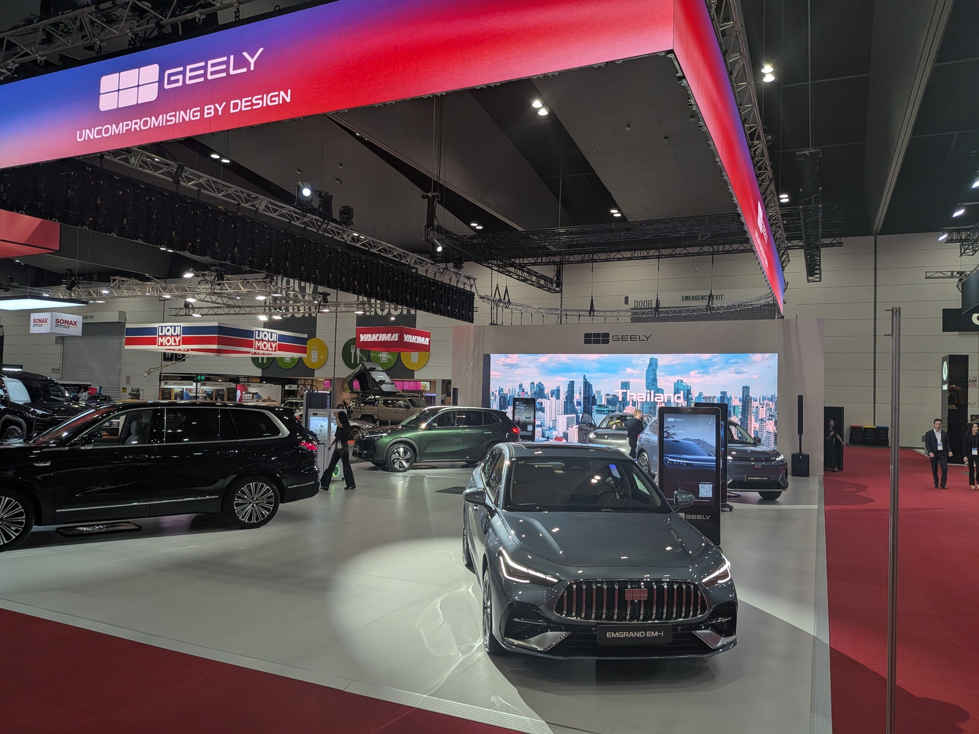 Geely exhibition space with overhead illuminated branding banner and vehicles arranged across display floor - Encore Event Technologies
