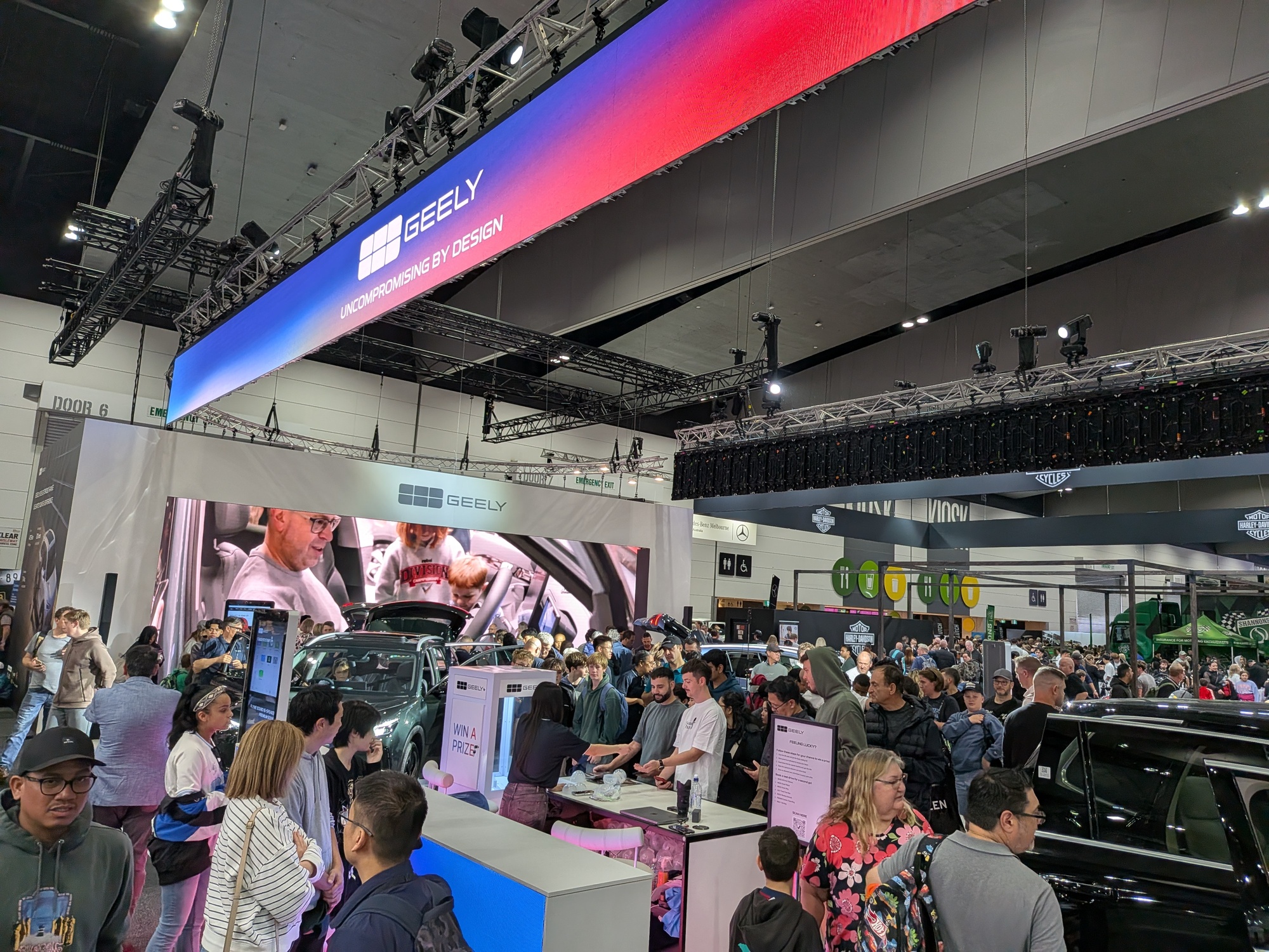 Crowded Geely stand with overhead “Uncompromising by Design” banner, LED screen content and visitors interacting with vehicles - Encore Event Technologies