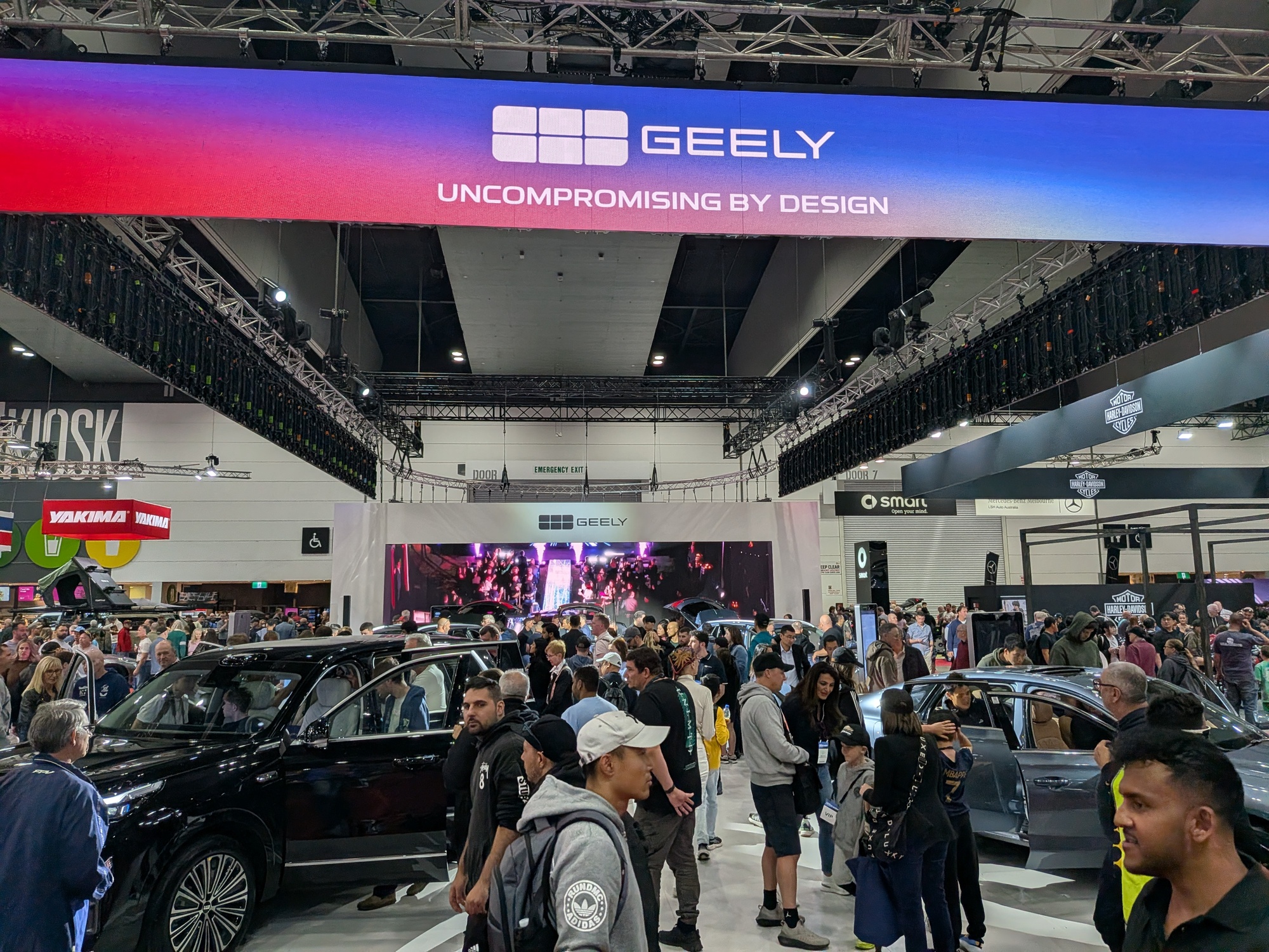 Crowded Geely stand under “Uncompromising by Design” overhead signage with visitors exploring vehicle displays - Encore Event Technologies