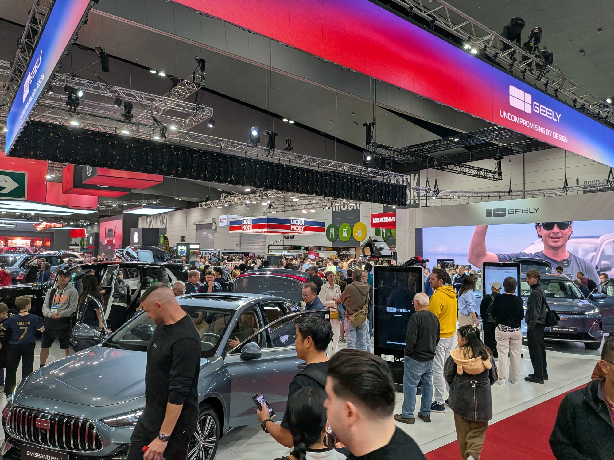 Active motor show environment with Geely vehicles, touchscreen kiosks and attendees interacting across exhibition floor - Encore Event Technologies