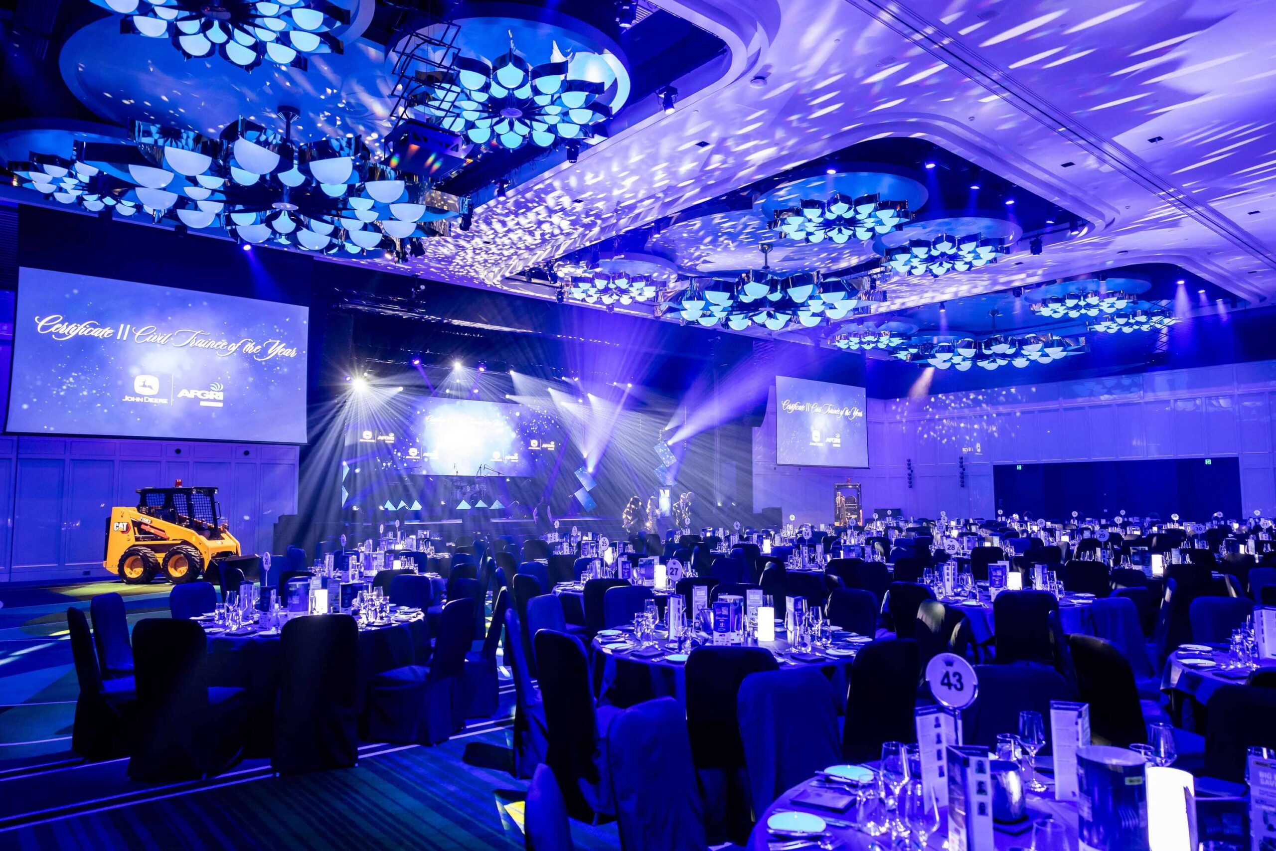 Wide view of banquet-style awards event at Crown Perth with stage lighting, production screens, and set tables ready for attendees – Encore Event Technologies
