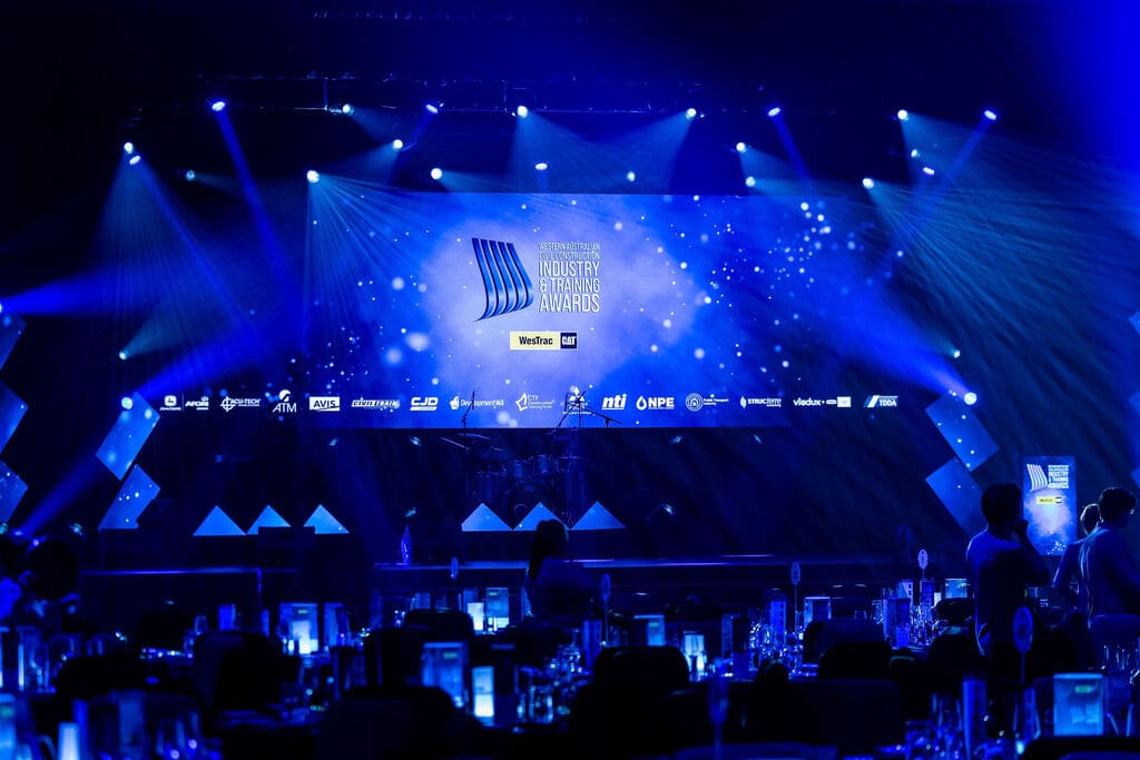 Stage presentation setup with illuminated LED screen displaying awards branding and dynamic lighting effects in a large event space – Encore Event Technologies