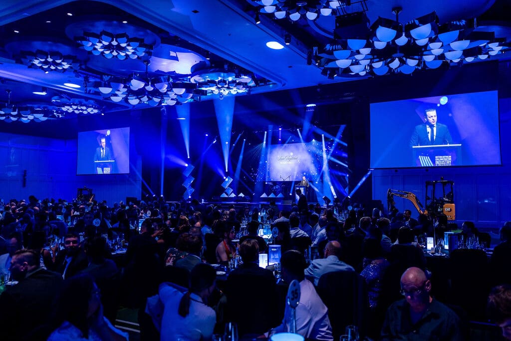 Awards ceremony in progress with presenter on stage, audience seated at banquet tables, and dual projection screens in a conference ballroom – Encore Event Technologies