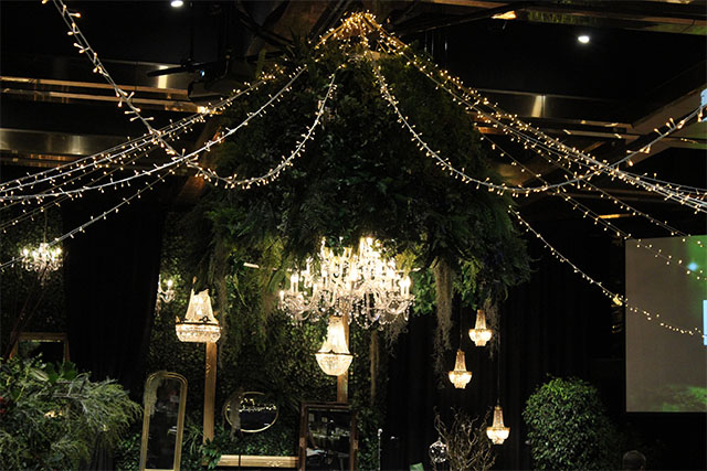Feature chandelier installation under a canopy of greenery and fairy lights creating a focal point in an event space – Encore Event Technologies