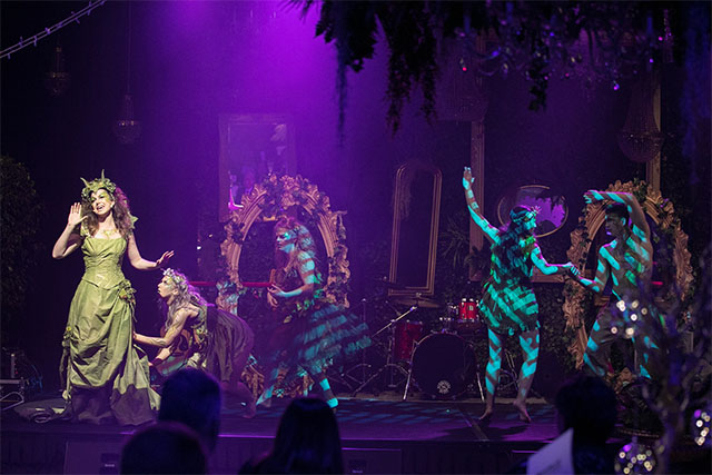 Stage performance with costumed performers in a forest-themed set with theatrical lighting and vintage props – Encore Event Technologies
