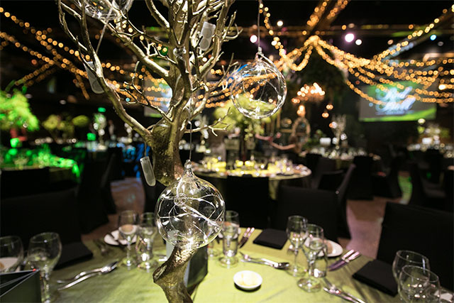 Close-up of a decorative tree centrepiece with hanging glass orbs and fairy lights on a formally set dining table – Encore Event Technologies