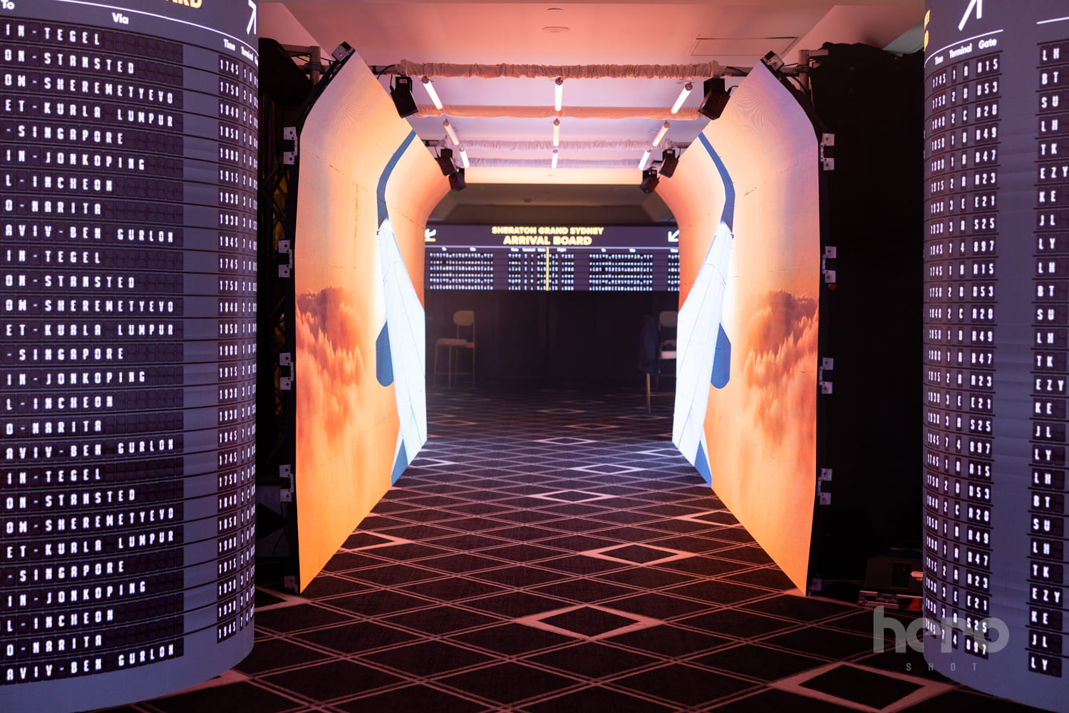 Airport-inspired event entrance at Sheraton Grand Sydney, featuring illuminated arrival boards, aircraft-themed tunnel walls and dramatic lighting leading into the venue - Encore Event Technologies