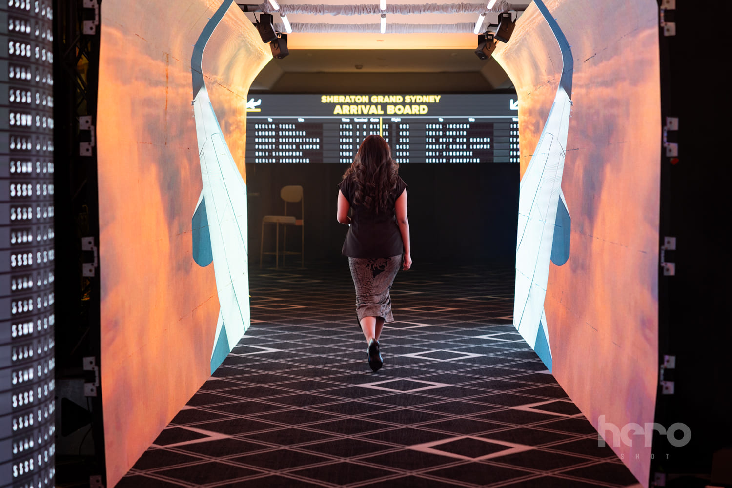 Guest walking through an immersive airport-themed entrance tunnel toward a Sheraton Grand Sydney arrival board display - Encore Event Technologies