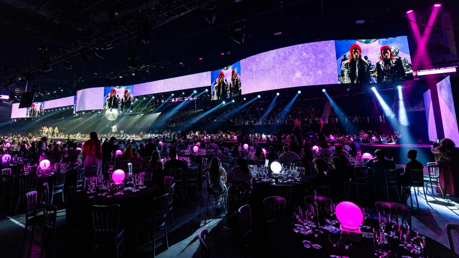 Two runway performers in sculptural costumes under dramatic arena lighting - Encore Event Technologies