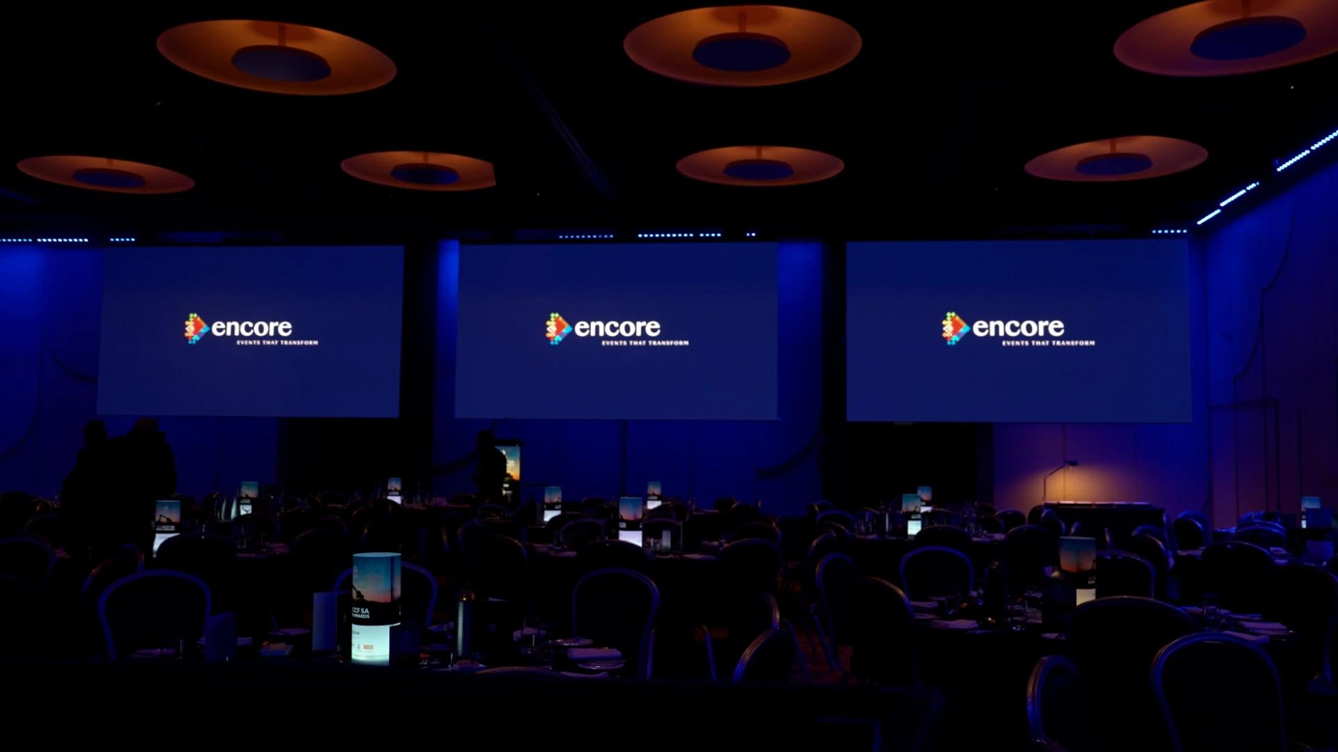 Encore branding displayed across large projection screens in a blue-lit awards ballroom - Encore APAC