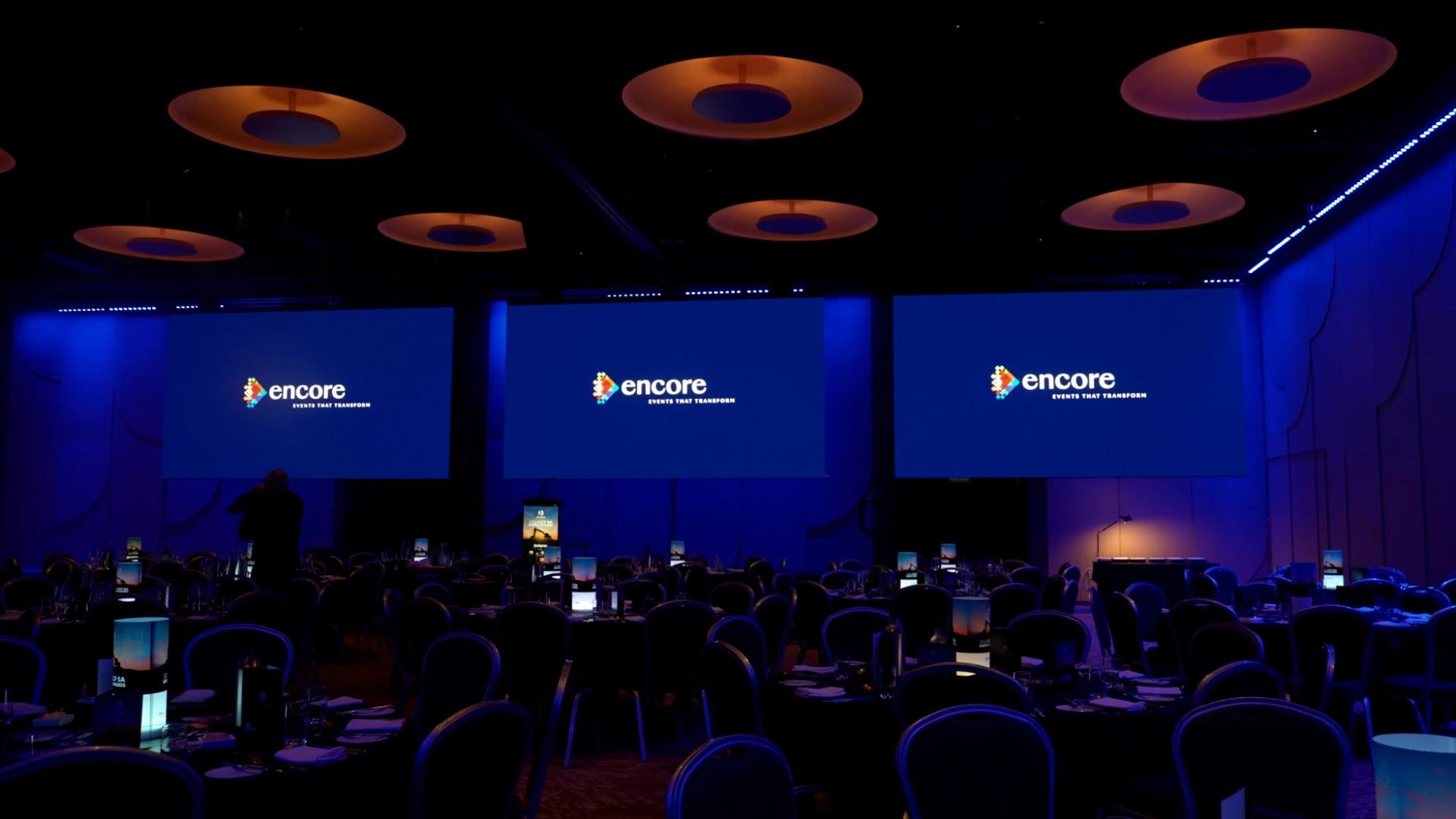 Encore branding displayed across large projection screens in a blue-lit awards ballroom - Encore APAC